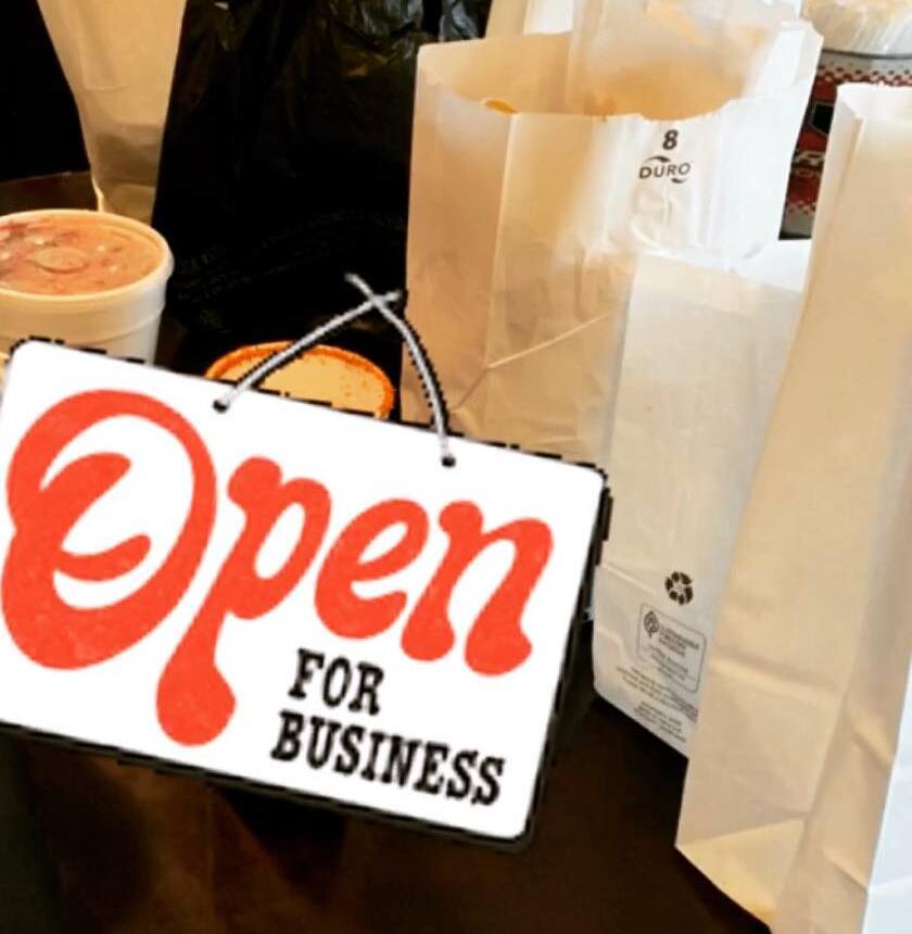 Su letrero rojo de "Open for Business" sobre bolsas de papel para llevar
